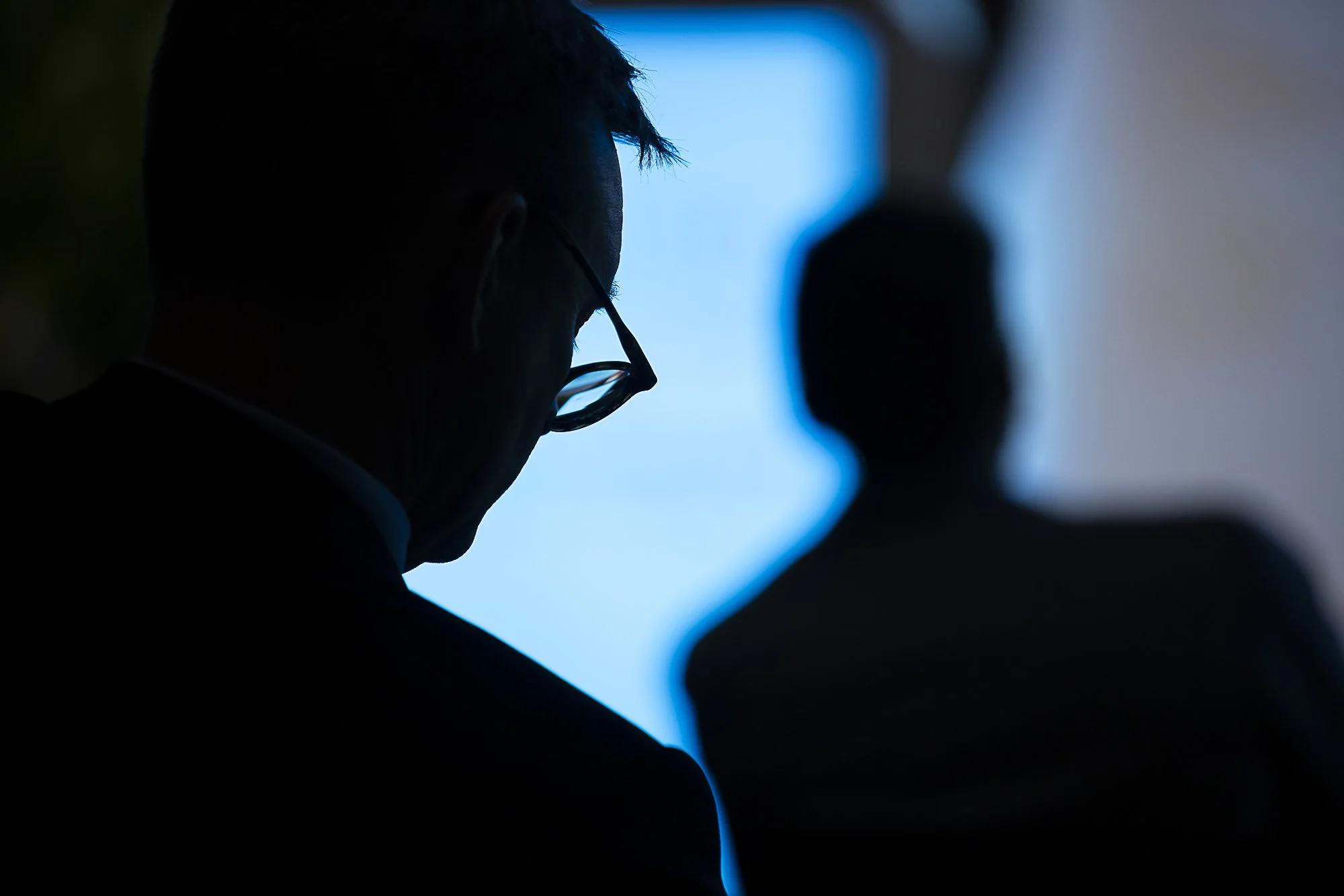 Silhouette of a person wearing glasses looking at a bright screen, with other individuals in the background.