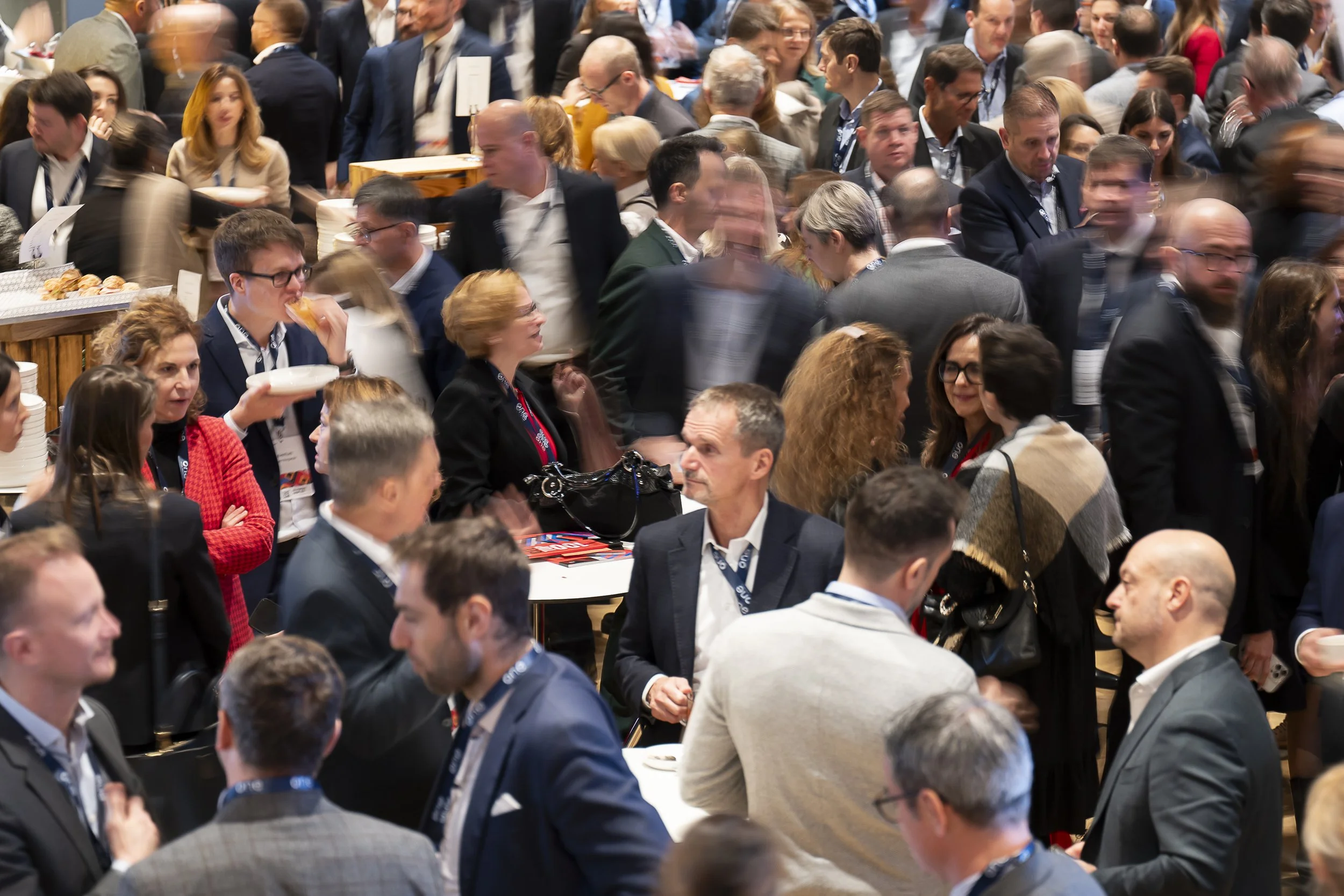 A crowded conference or networking event with many professionals in business attire, mingling and engaging in conversations.