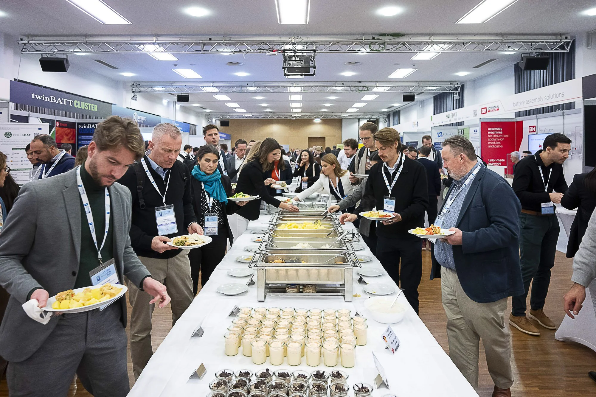 People at a buffet table serving themselves food at a conference or event, with various dishes and desserts displayed.