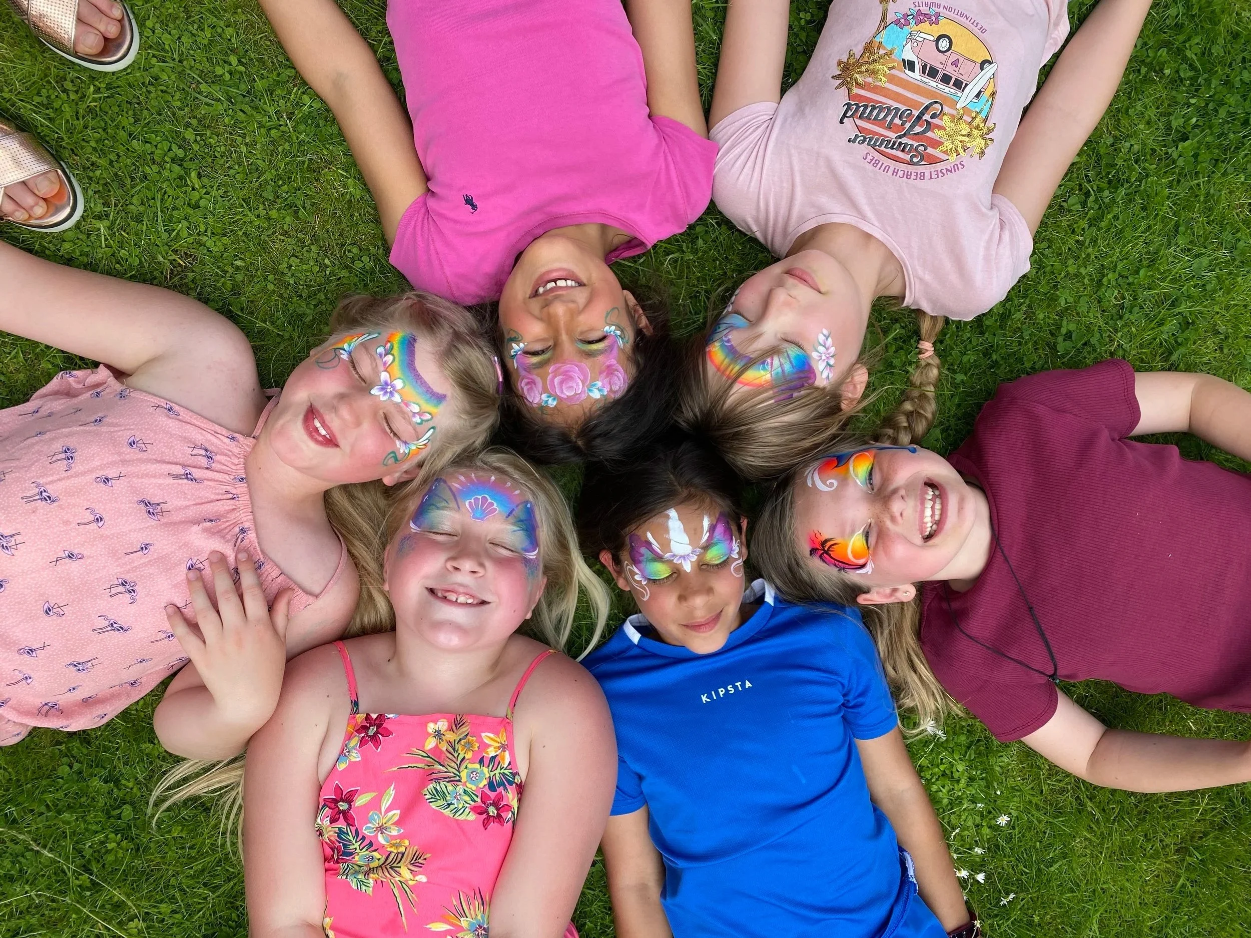 6 girls lying on the grass with face paints