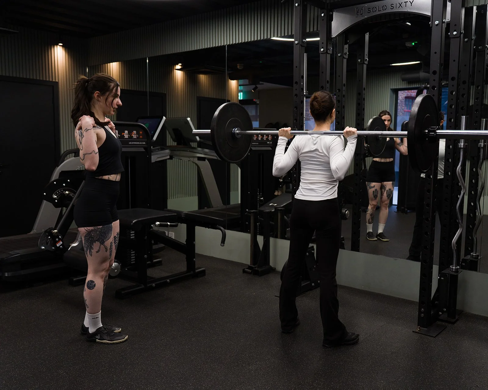 Nicolina in the gym coaching the back squat bar position to a client