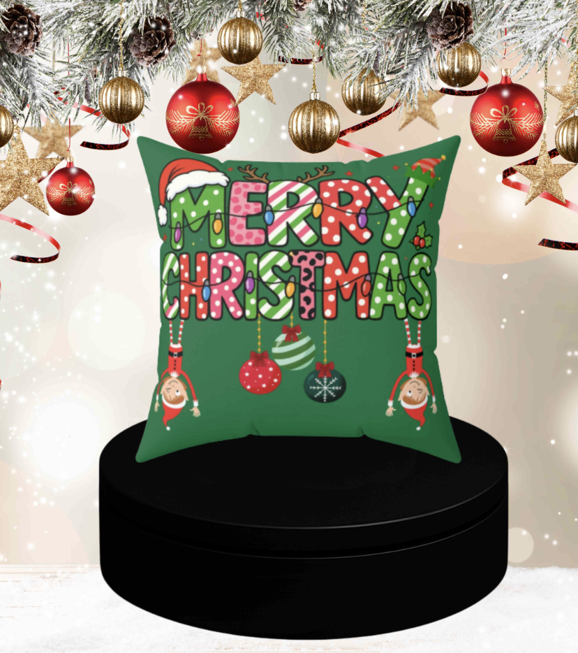 Decorative Christmas pillow with colorful text, hanging ornaments, and Christmas-themed characters, set on a black round platform with holiday decorations overhead.