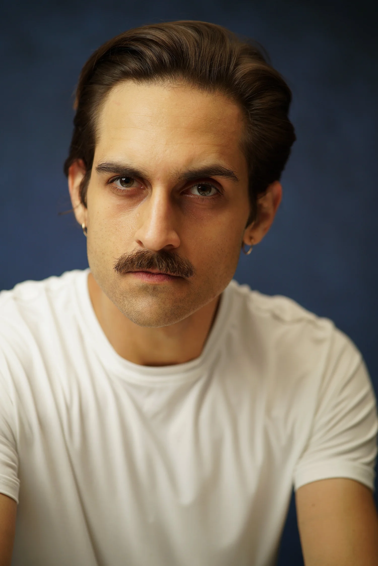 Milan Babi serious leaned-in mustache headshot in white shirt