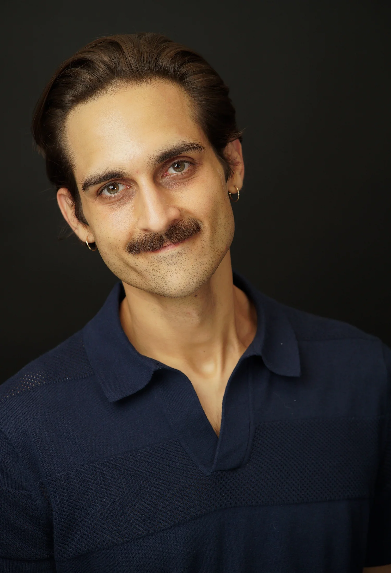 Milan Babi bashful smiling headshot in navy polo with mustache