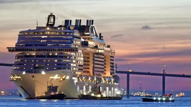Un grand navire de croisière à quai avec un pont suspendu en arrière-plan, lors du coucher du soleil.