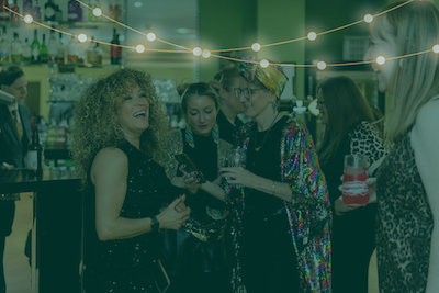 A group of people gathered at a bar dressed in sparkly clothes. They are holding drinks and laughing
