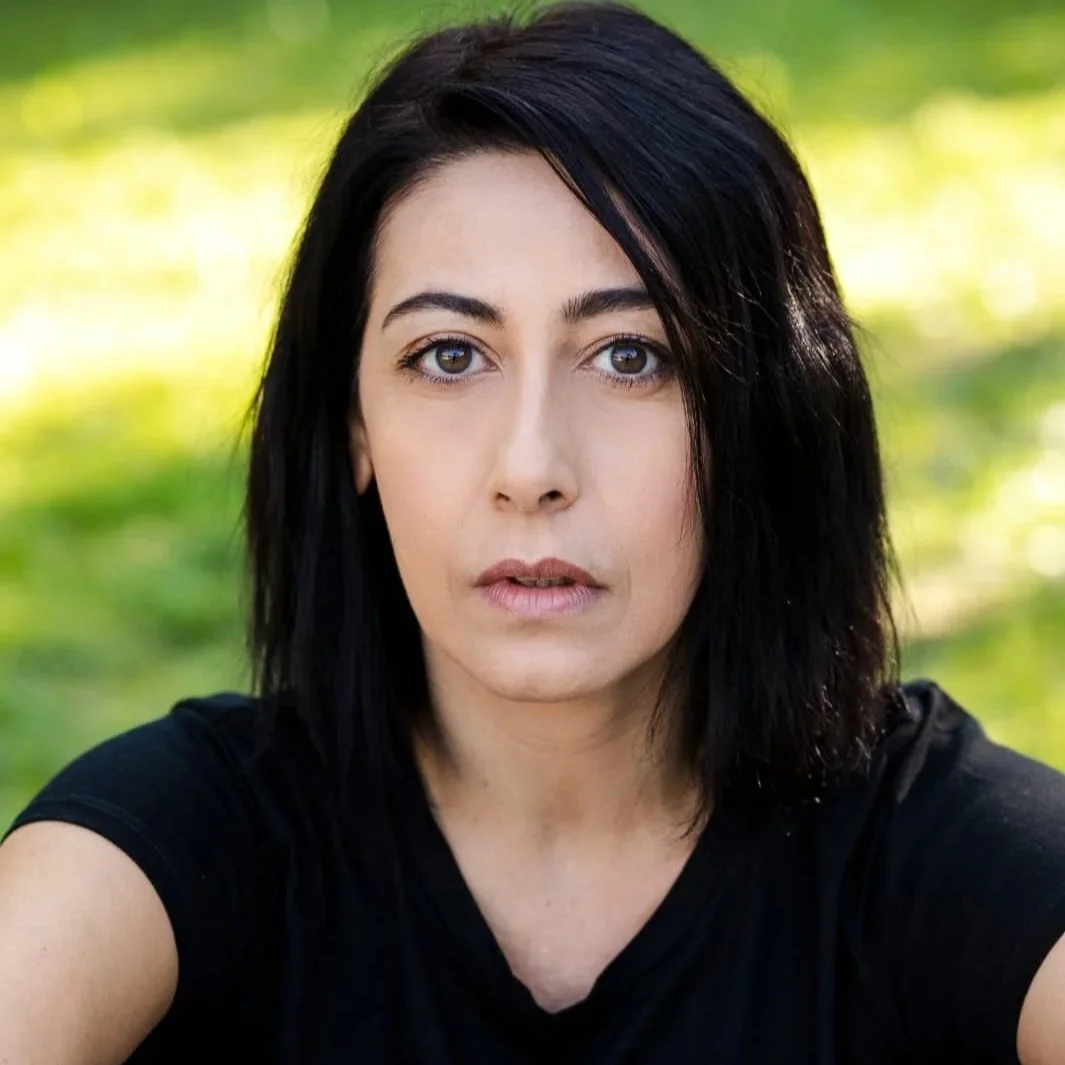 Ragazza con capelli neri, espressione seria, sfondo verde sfocato