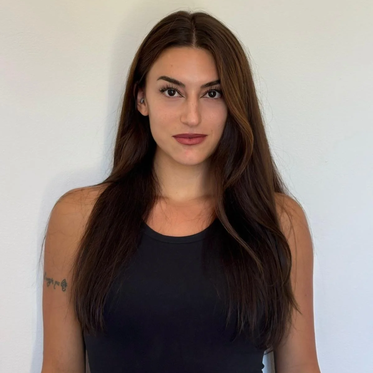 Donna con capelli lunghi e castani, vestita con top nero, che si trova davanti a una parete con porte avvolgibili bianche.