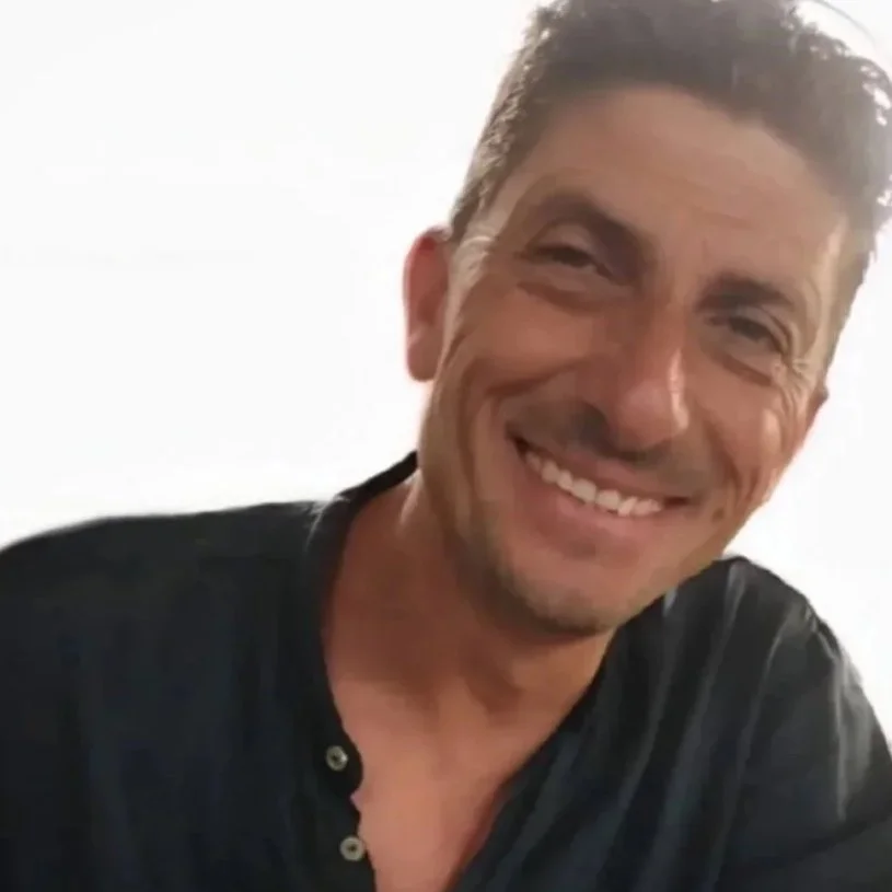 Uomo sorridente con capelli scuri e maglietta nera.