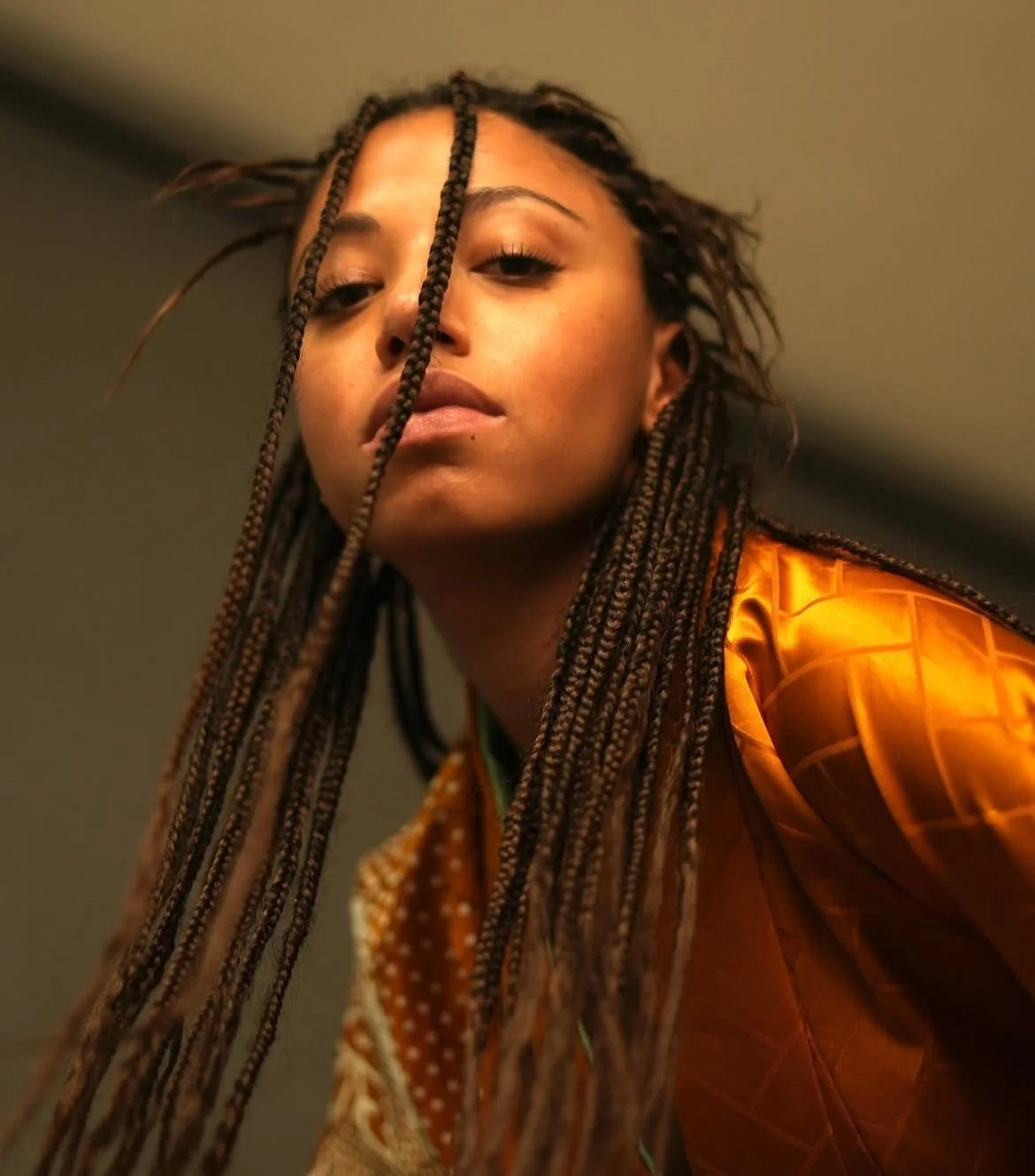 Ragazza con trecce, vestita con una giacca arancione, guarda verso la telecamera.