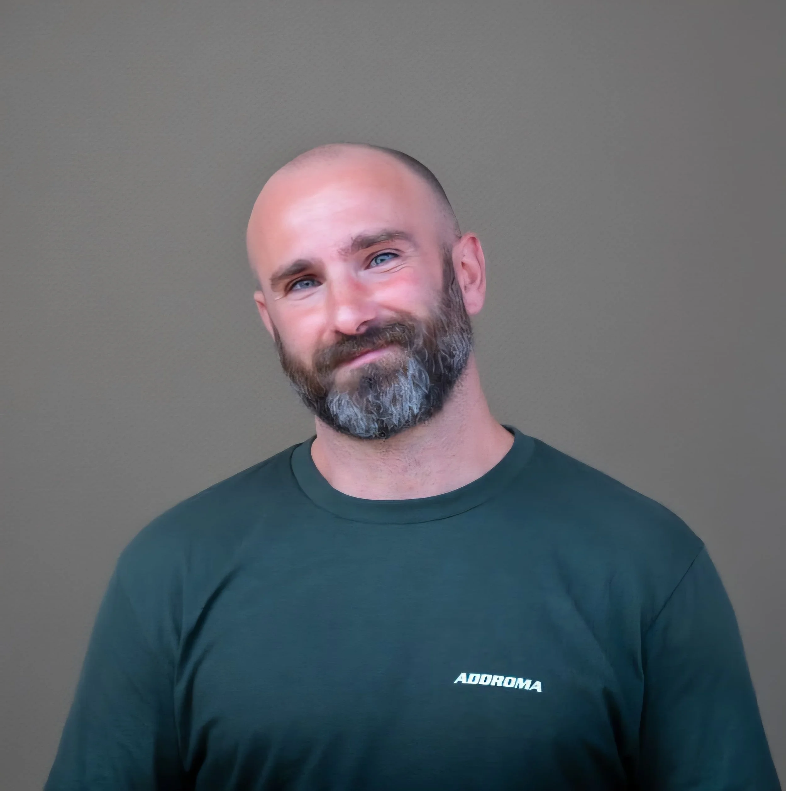 Uomo con barba e testa rasata che indossa una maglietta verde scuro con la scritta "ADROMA", sfondo grigio