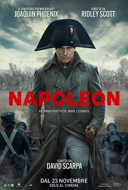 Locandina del film 'Napoleon' con Joaquin Phoenix come protagonista, indossa un grande cappello napoleonico e uno cappotto militare, sullo sfondo si vedono soldati e cannoni in battaglia, con un cielo nuvoloso.