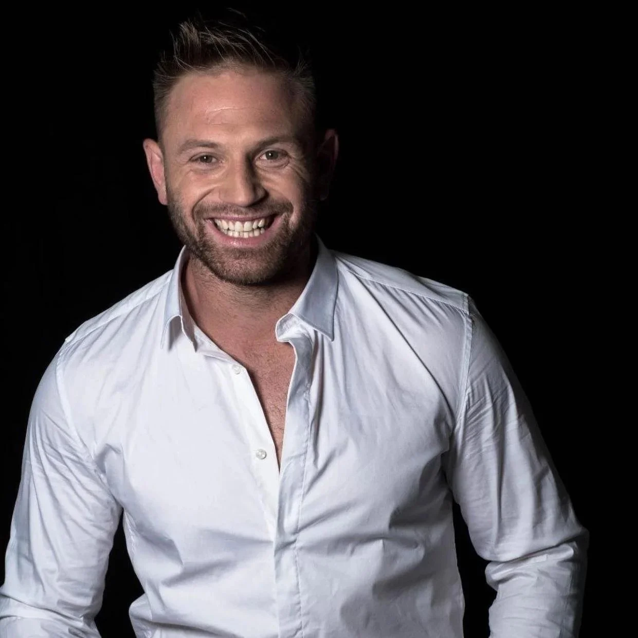 Uomo sorridente con camicia bianca, sfondo nero.