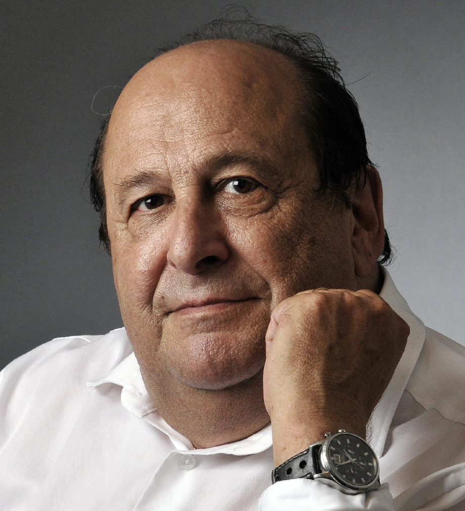 Portrait d'un homme âgé portant une chemise blanche et une montre noire, posant avec la tête appuyée sur sa main.