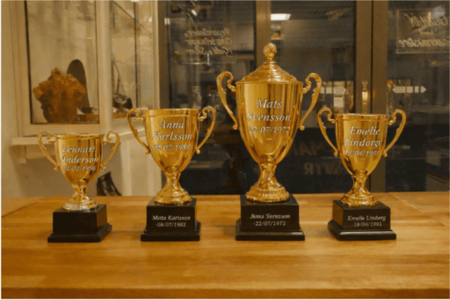 Bild på pokaler som har blivit graverade för hand med olika namn och tysnitt