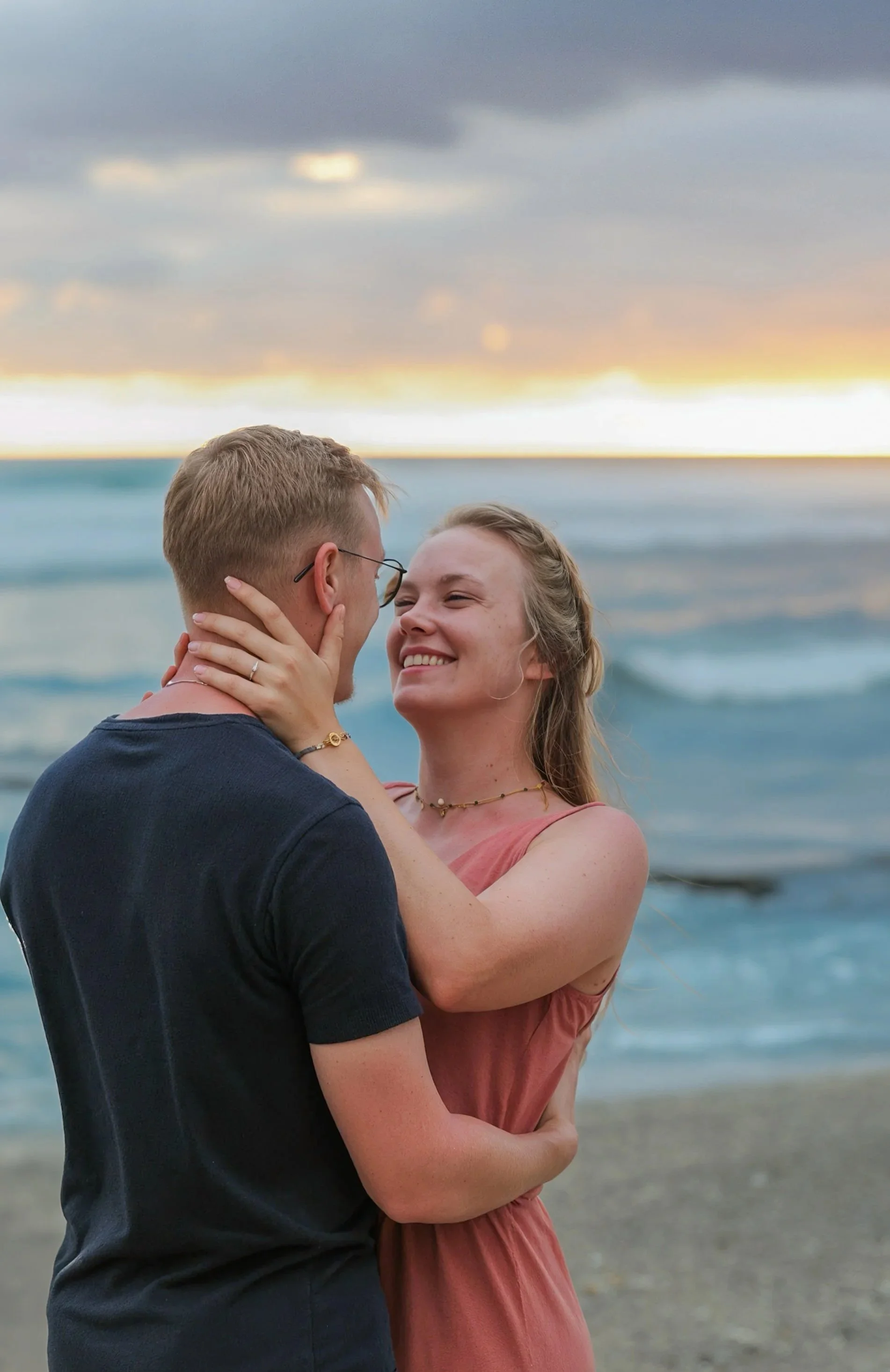 Un couple s'embrassant près de la mer au coucher du soleil, avec un ciel nuageux.