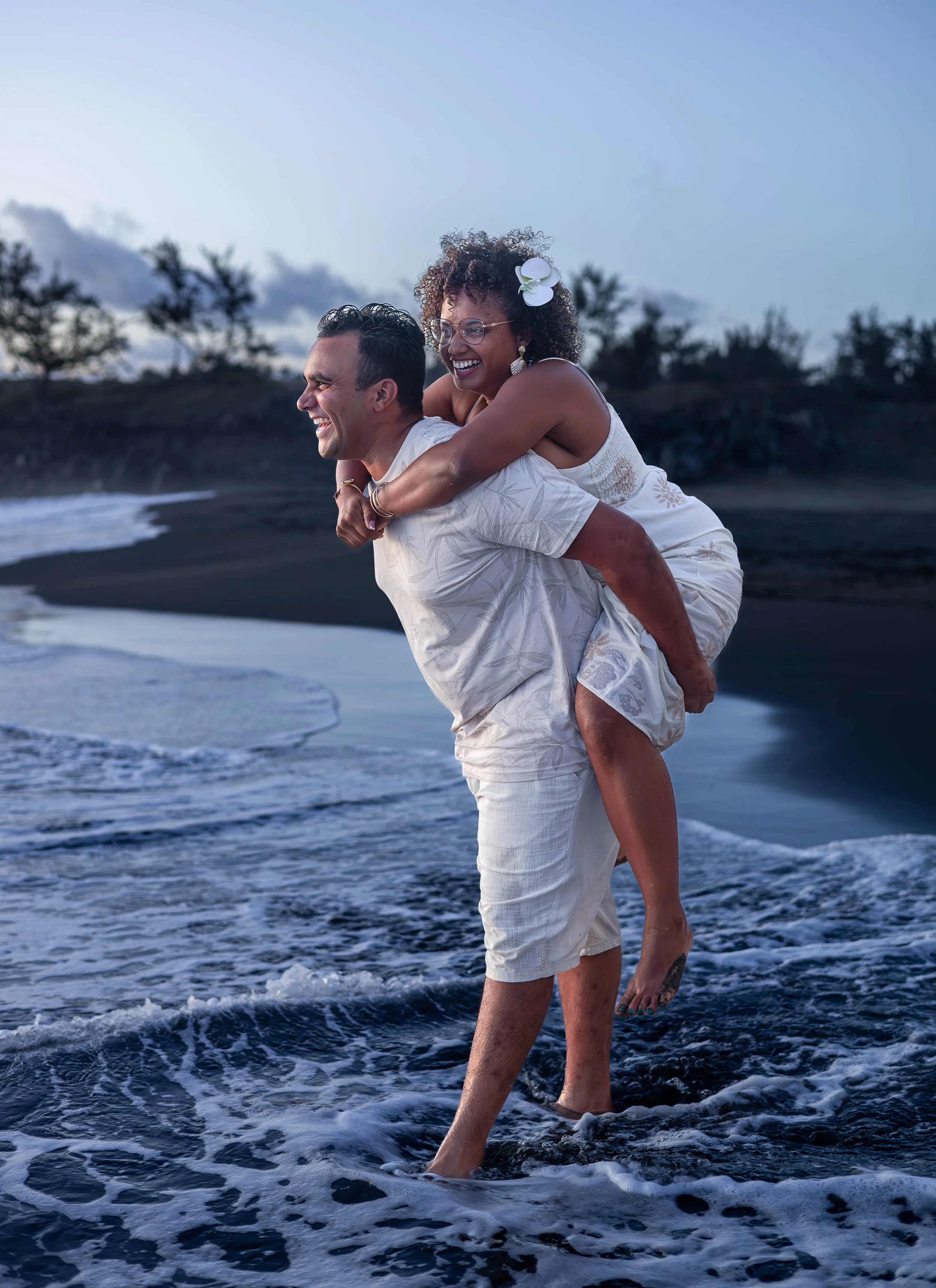 Un couple joyeux se promène sur la plage au coucher du soleil, avec des paysages naturels en arrière-plan.