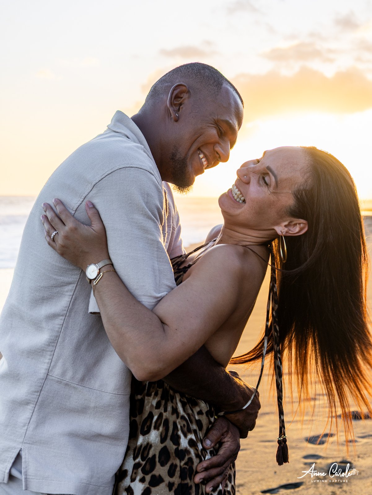 Un couple souriant, s'embrassant à la plage au coucher du soleil.