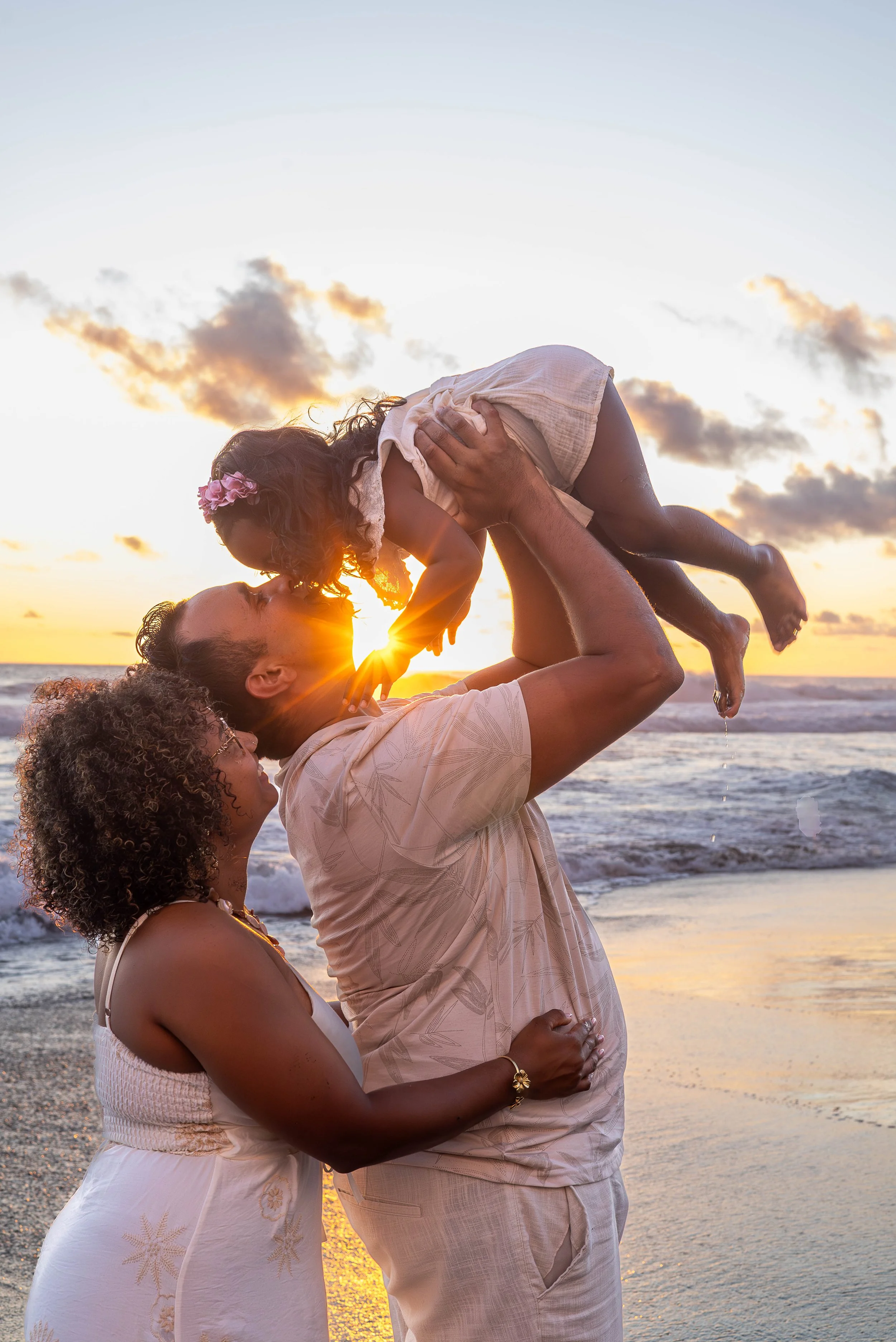 Une famille joyeuse avec un père levant une fille au coucher du soleil sur la plage.