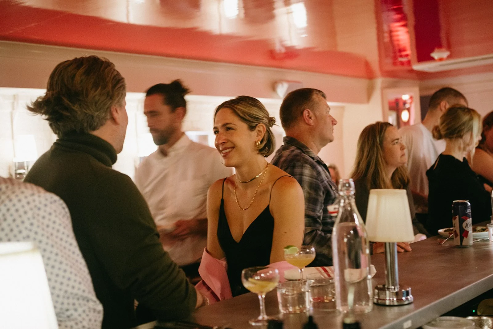 People socializing at a bar or restaurant with drinks and warm lighting.