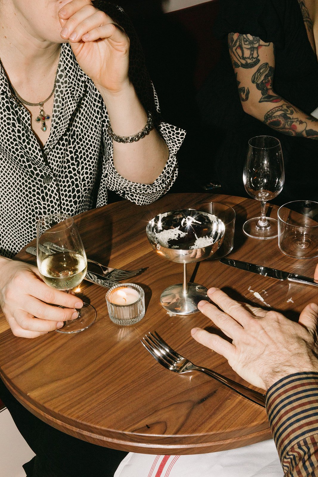 People seated at a wooden table with wine glasses, a candle, and a cocktail.