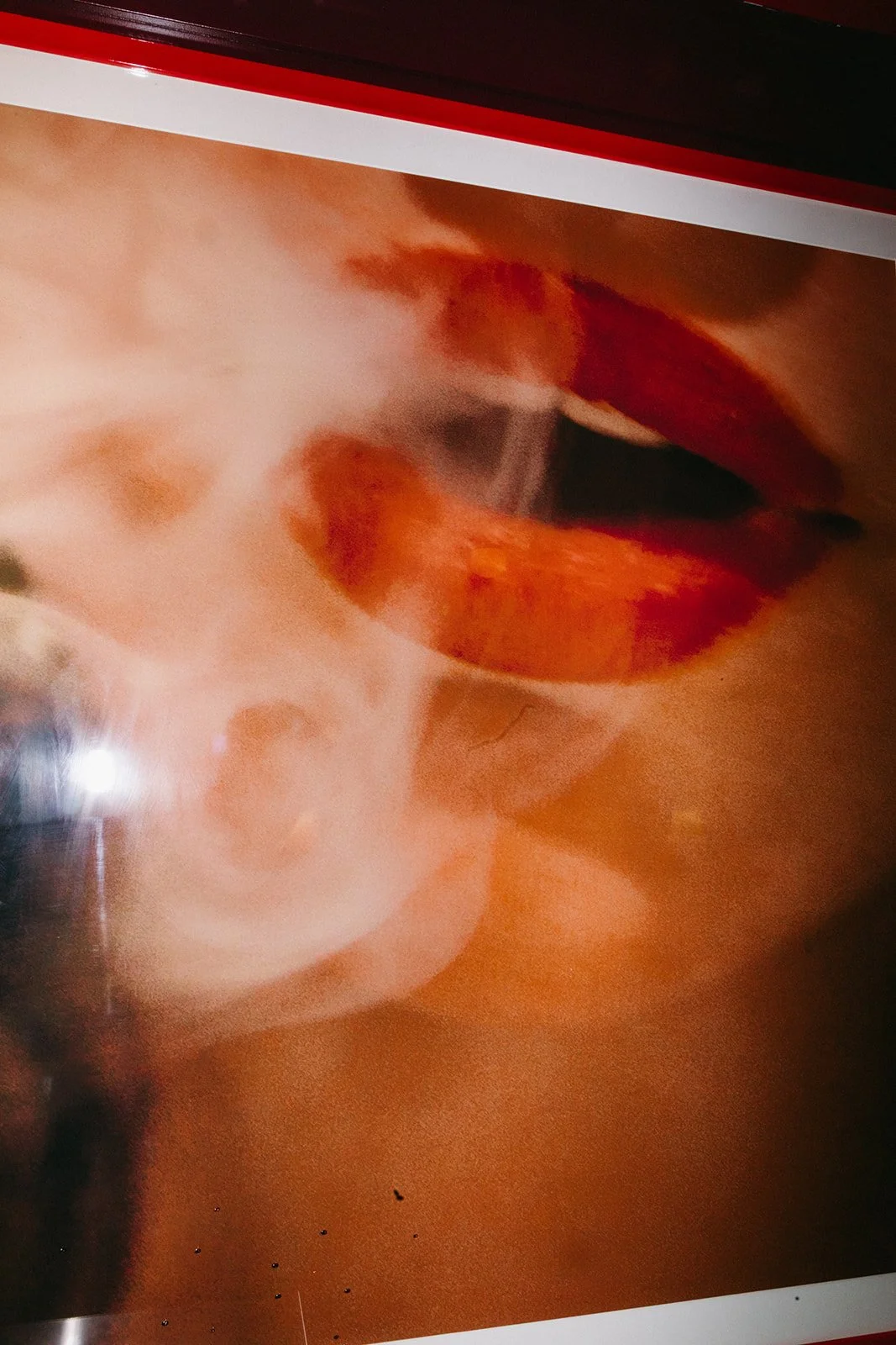 A close-up of a glossy magazine-style image featuring a woman with red lips and smoke around her face.