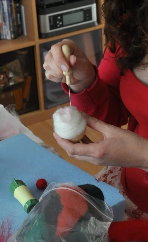 Person using a small tool to needle felting a ball of white wool.