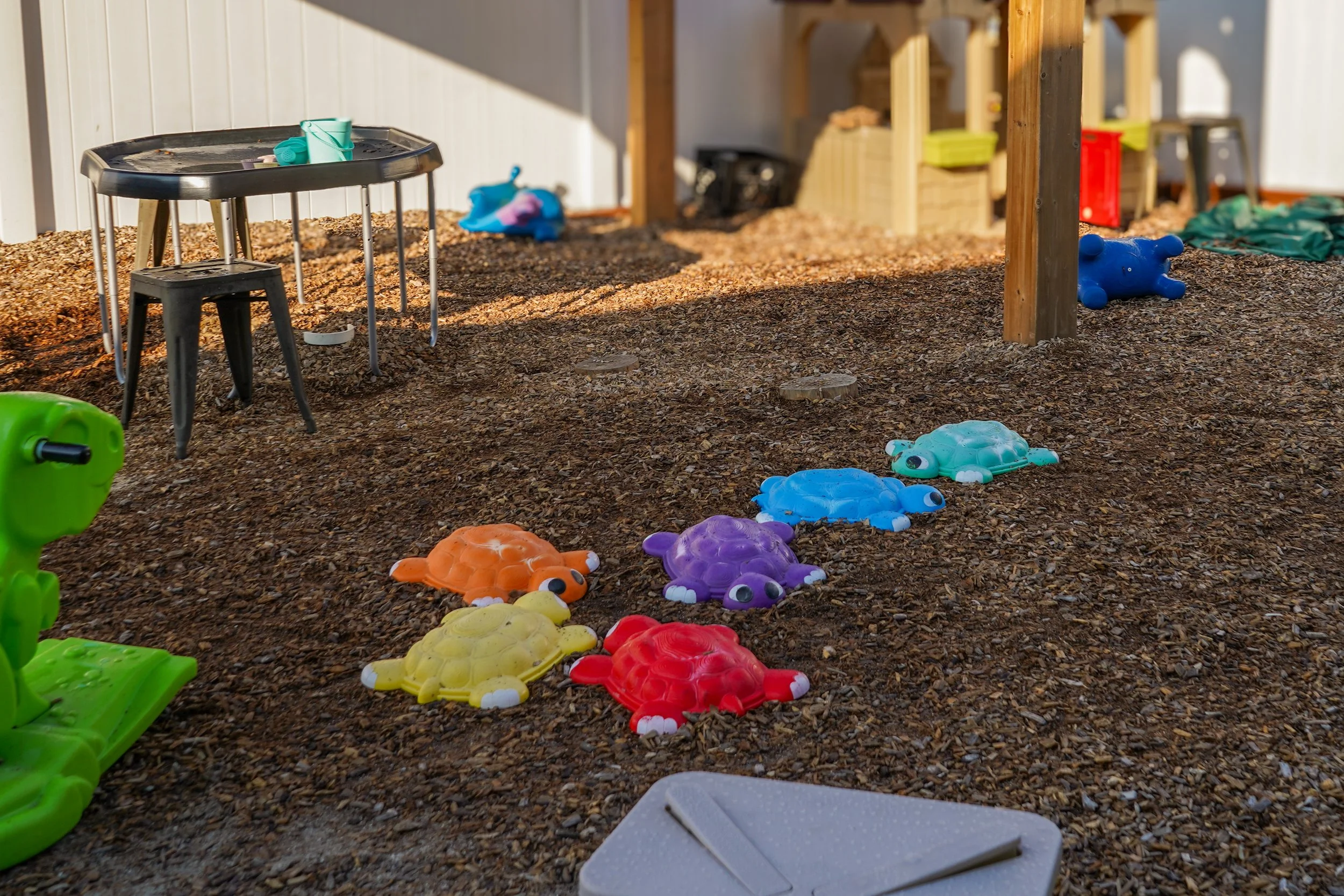 Colorful turtle-shaped toys on a gravel ground in a backyard with playground equipment and wooden structures.