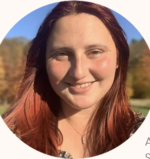 Close-up of a young woman with red hair smiling outdoors in autumn setting.