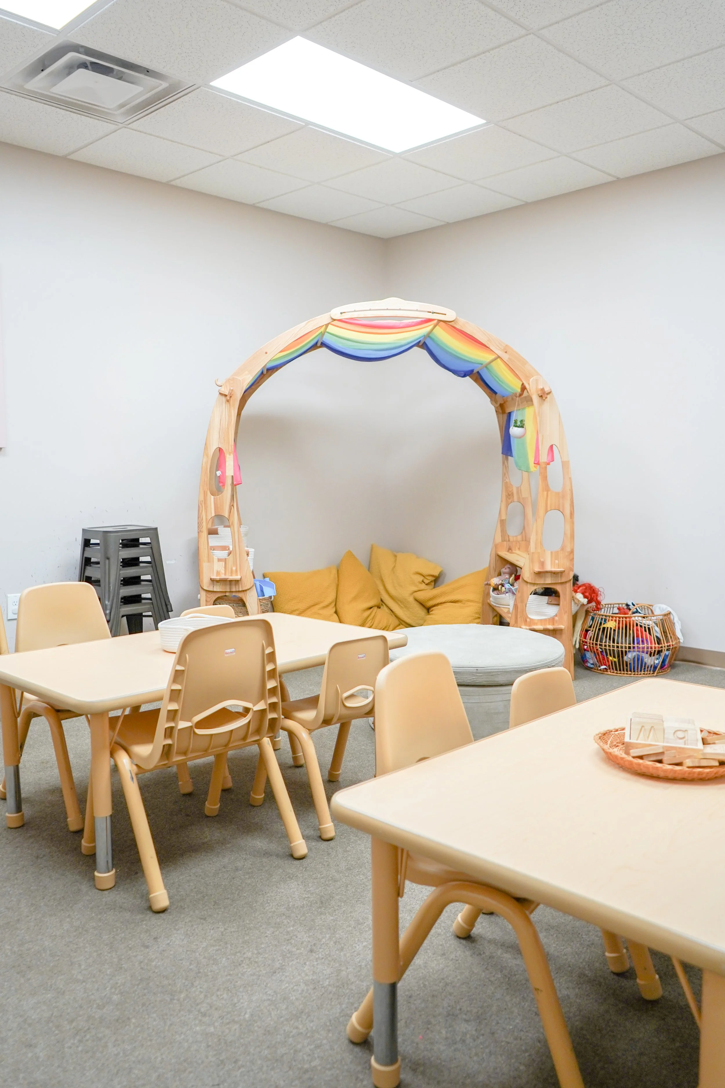 Kids' playroom with a rainbow-colored teepee and small tables and chairs.