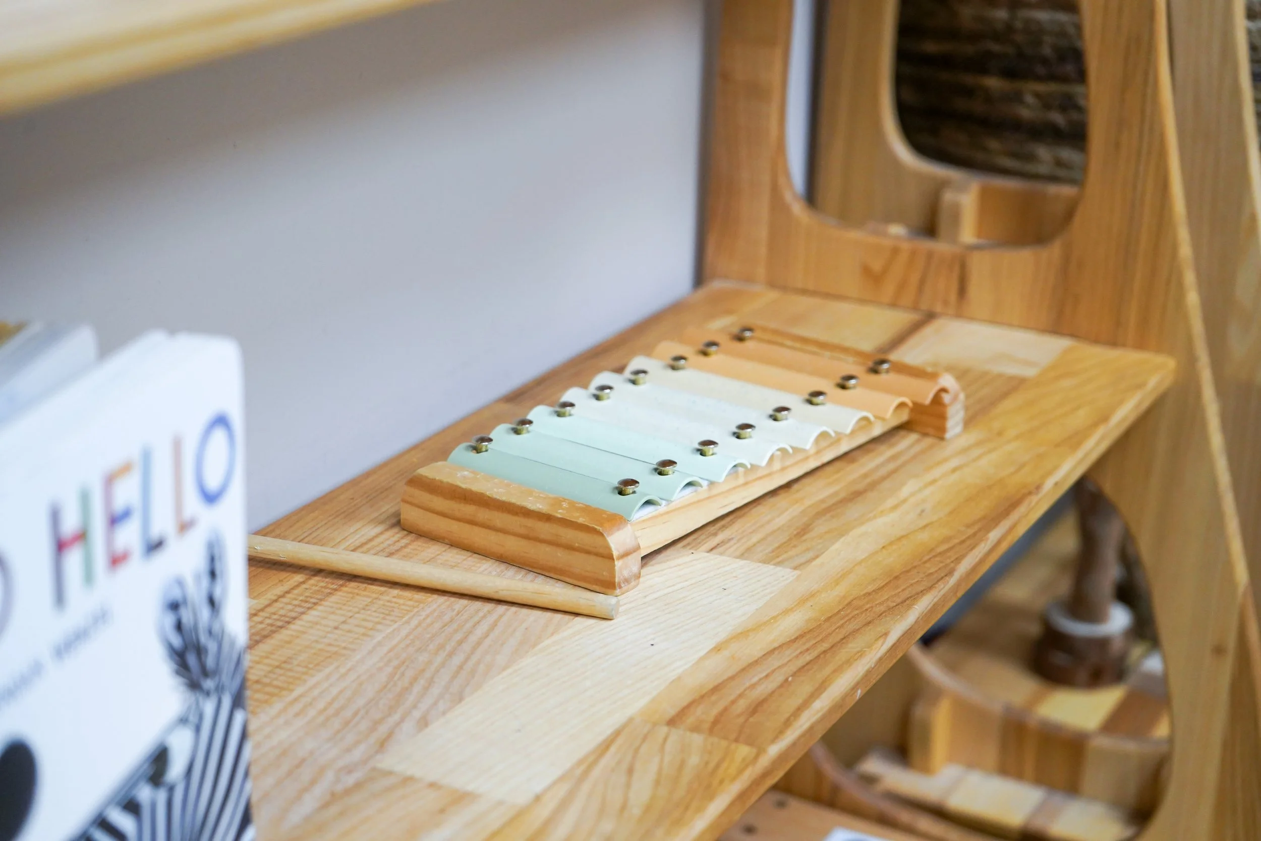 Wooden desk with a small xylophone, a pointer stick, and a partial view of a picture book titled 'Hello'.