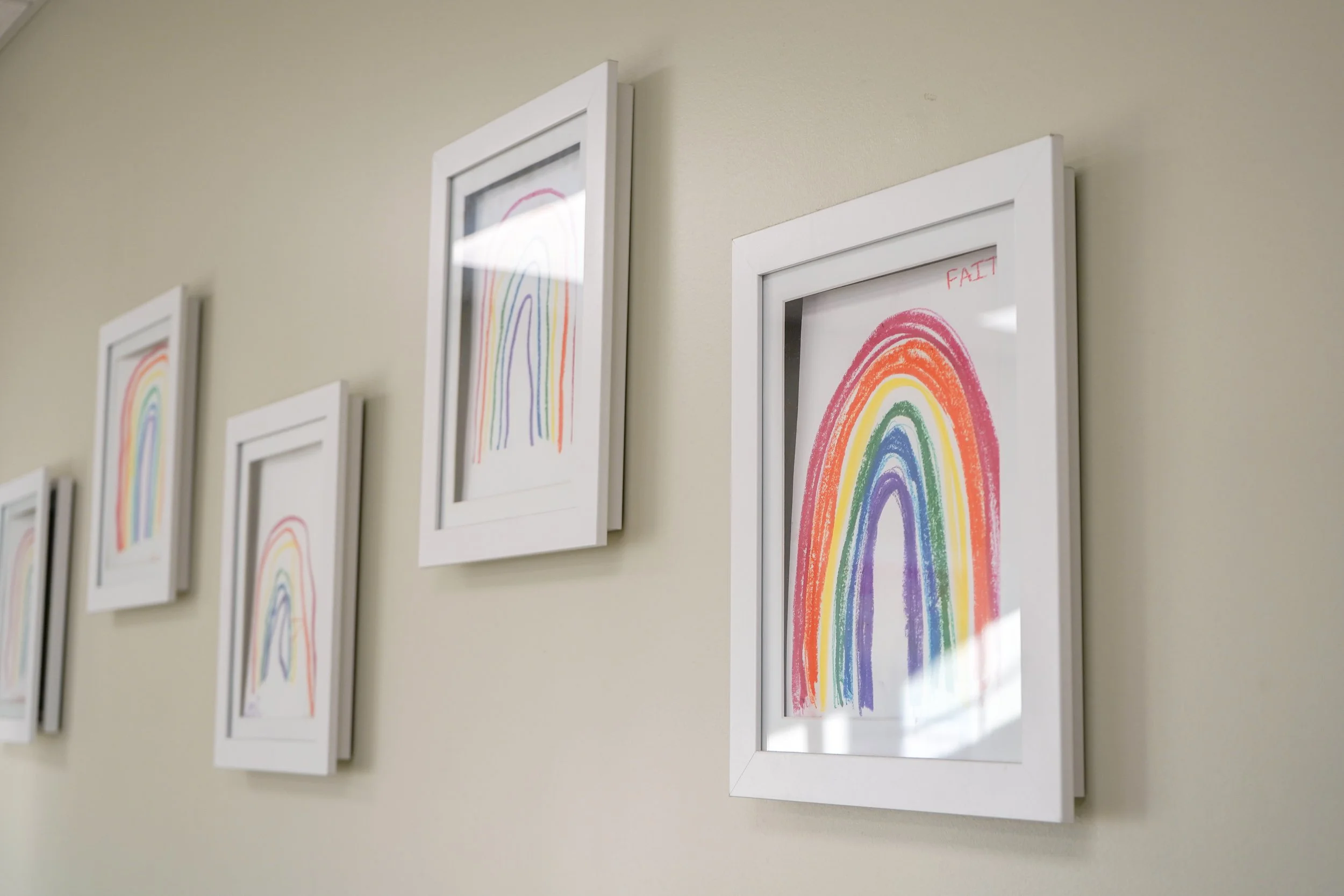 A series of framed drawings of rainbows with rainbow-colored arcs on a light-colored wall.