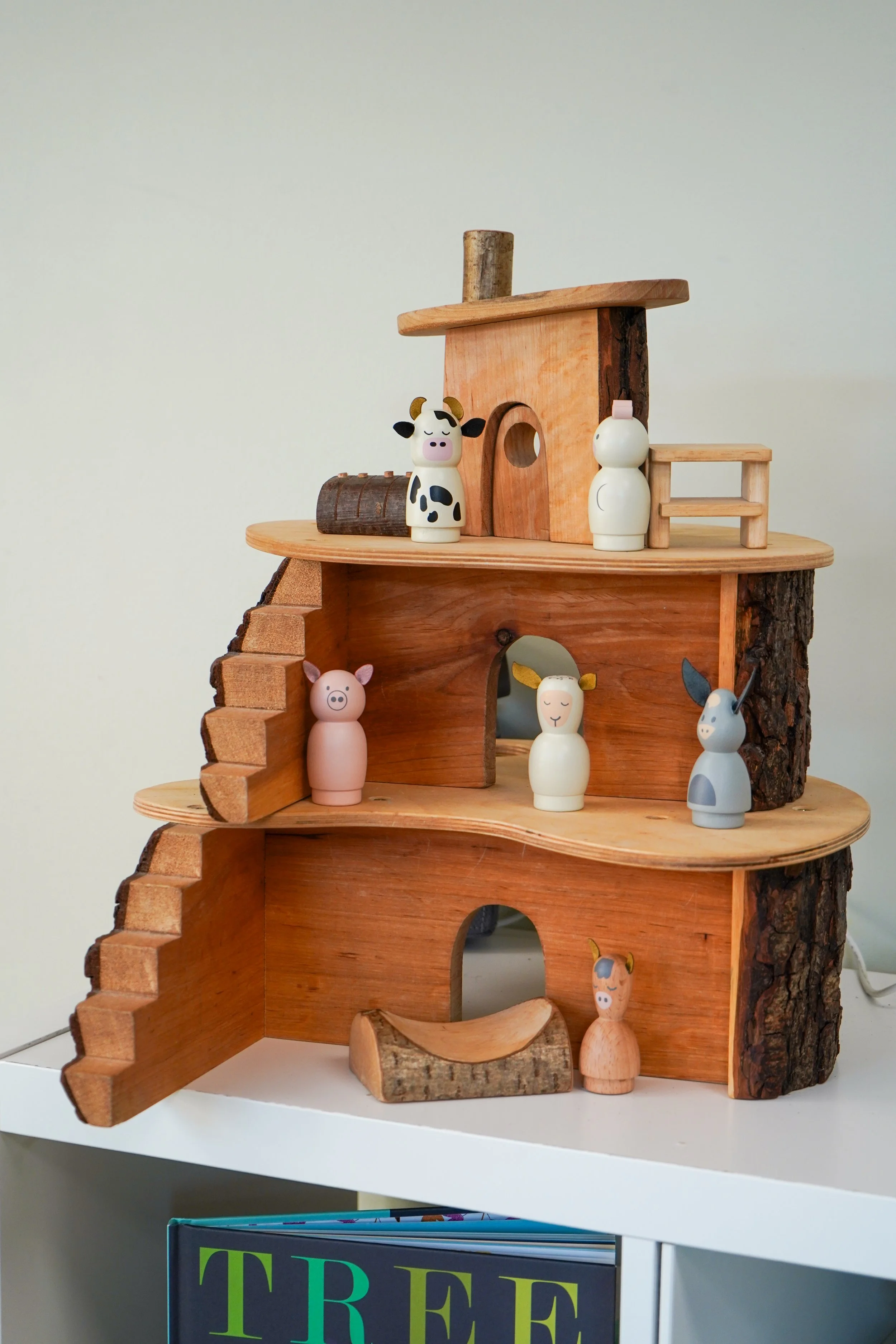 Wooden toy barn with animal figurines including a cow, pig, sheep, horse, and rabbit, placed on a white shelf.