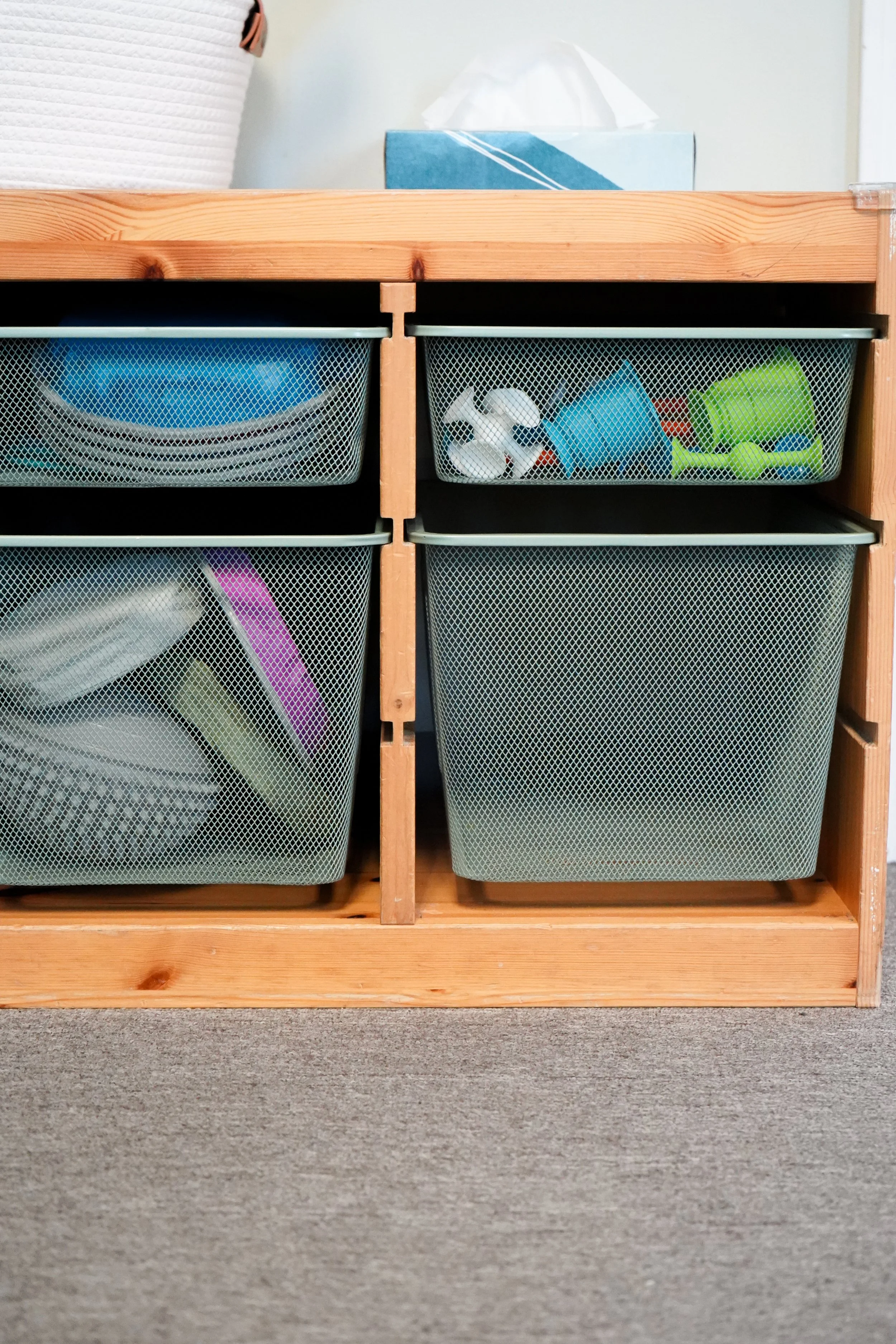 Wooden storage unit with four mesh baskets containing various household items like dishes, toys, and containers.