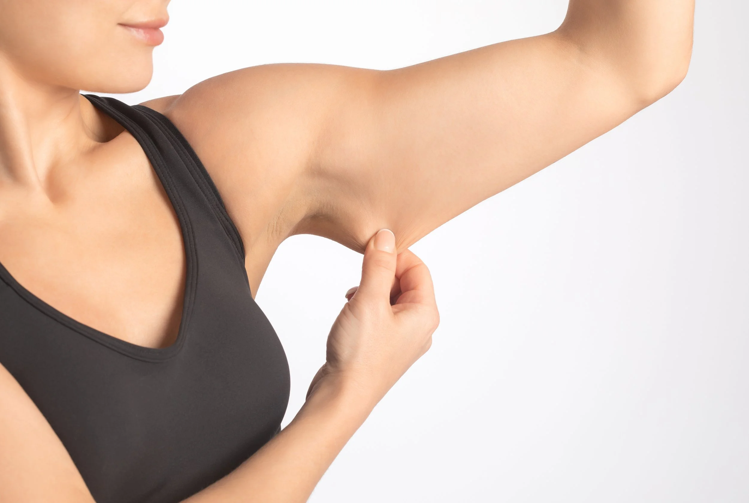 Une femme en débardeur noir examine son aisselle droite.