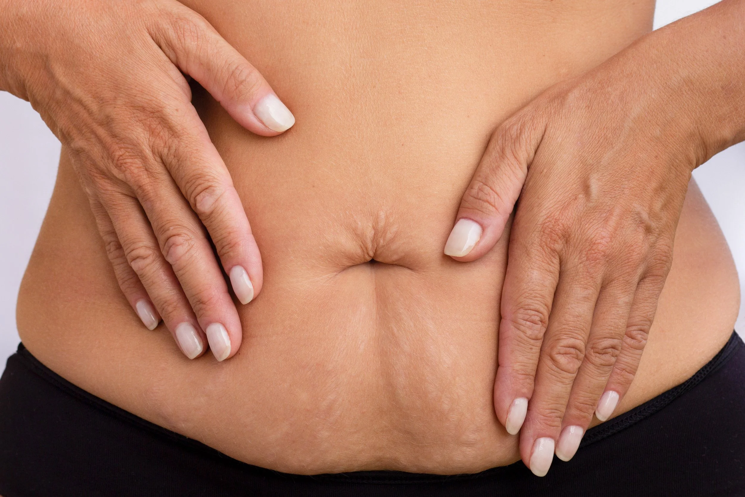 Les mains d'une personne touchent son abdomen nu, mettant en valeur l'ombilic, avec des ongles soignés.