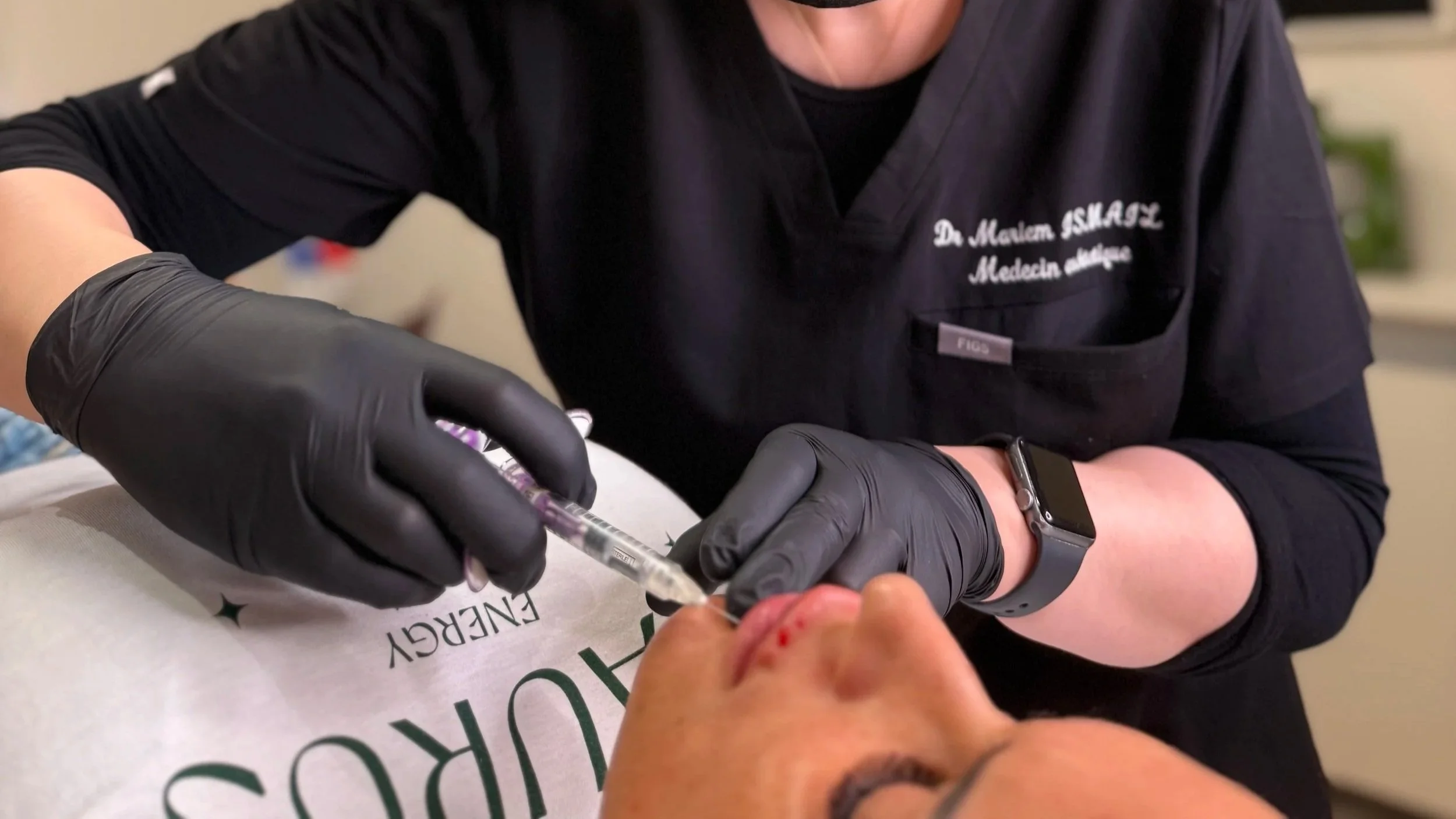 Un professionnel en blouse noire et gant noir administre une injection à une personne allongée.