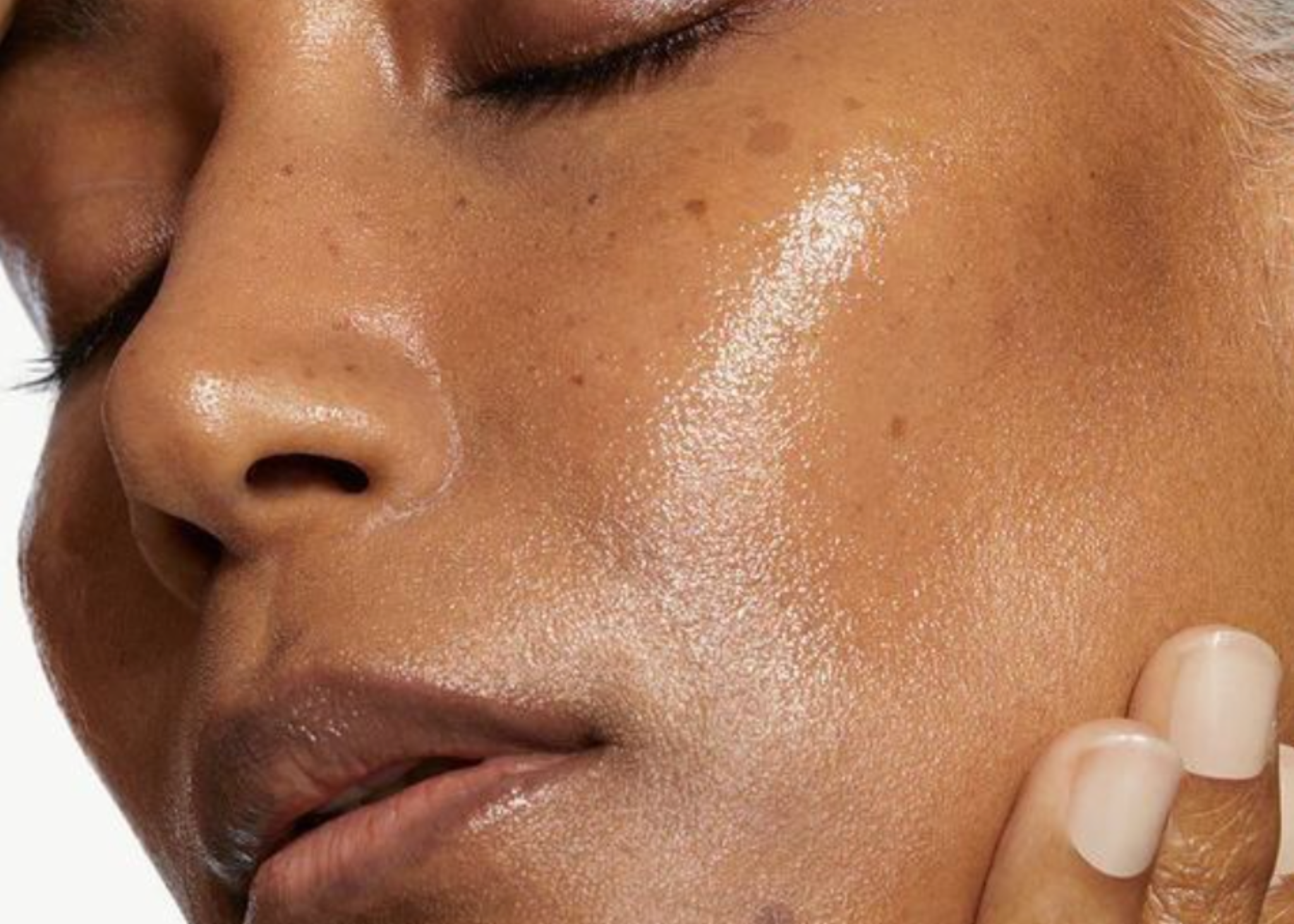 Portrait en gros plan d'une femme aux peaux foncée et maquillée, touchant doucement sa joue avec ses doigts.