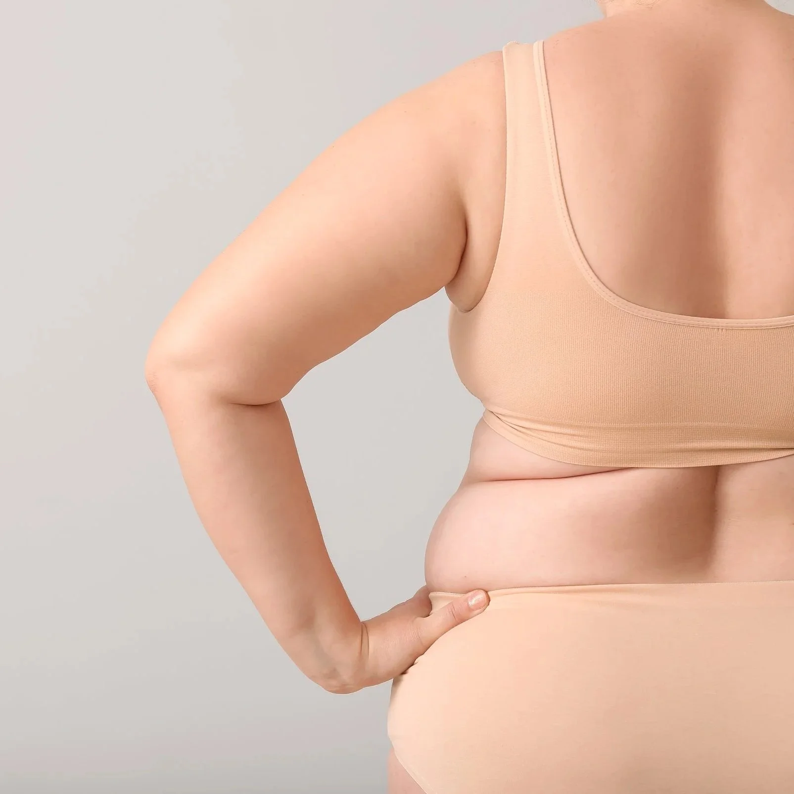 Personne portant un vêtement beige, vue de côté, avec la main sur la hanche, montrant la silhouette.