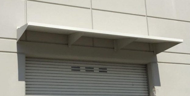 Close-up of a white building exterior with a metal overhang canopy hood and a closed gray rolling steel door.