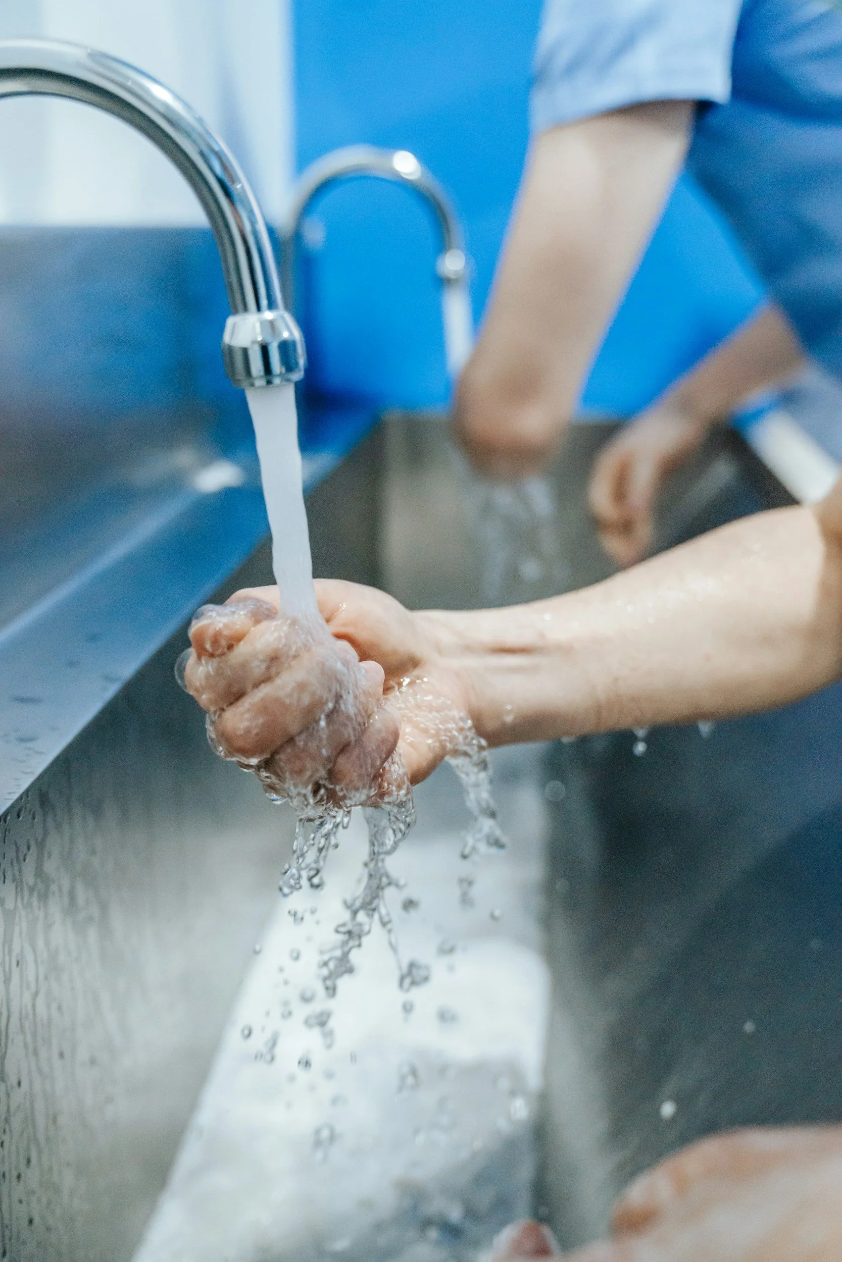 Person washing their hands under running water in a stainless steel sink.