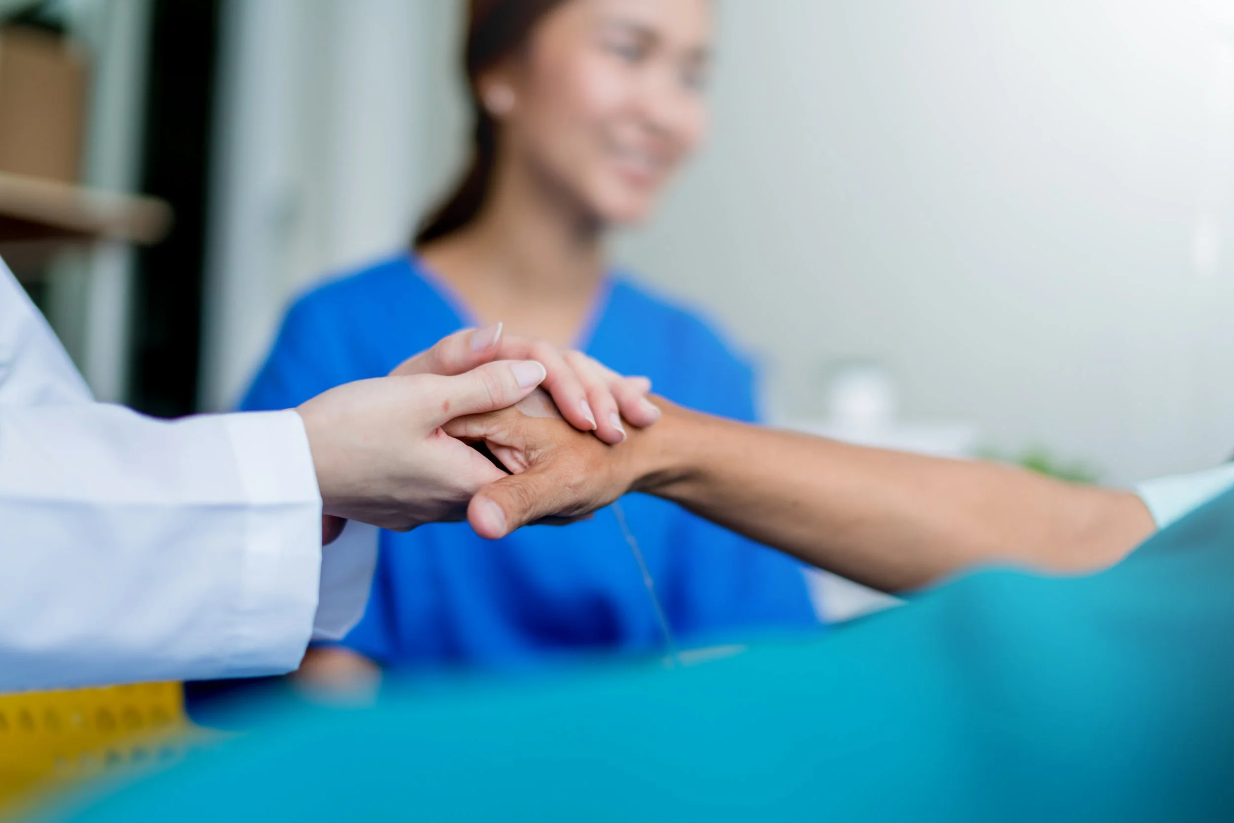 A healthcare professional holding a patient's hand during a medical examination or treatment in a clinical setting.