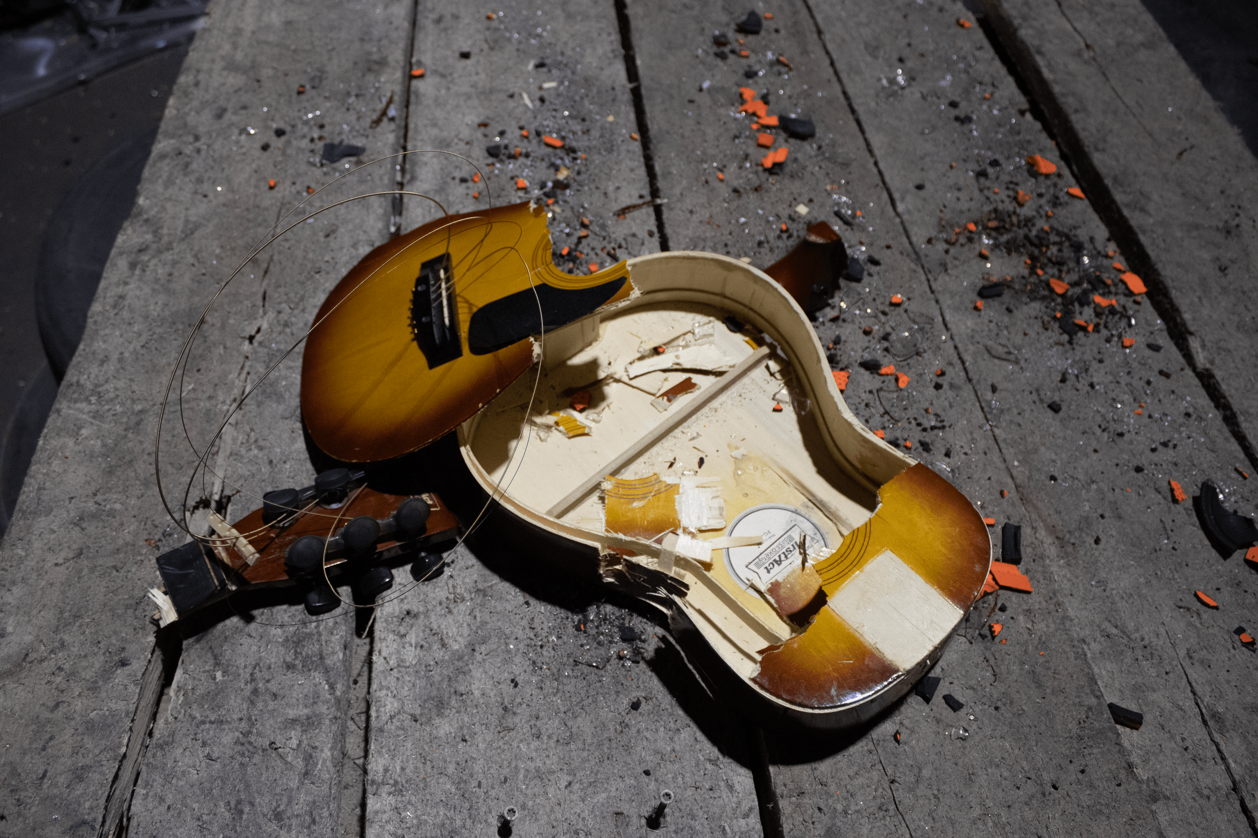 Broken acoustic guitar lying on a sidewalk, with scattered debris and parts around it.
