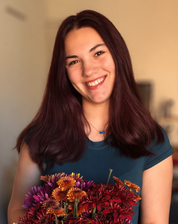 Photo of Syeirra Todaro, the designer; she has a triangular face shape, a bright smile, and shoulder-length red-brown hair.