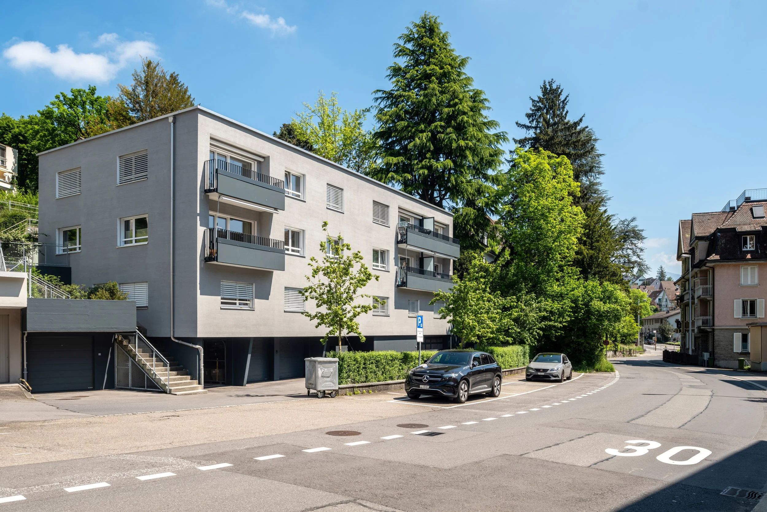 St. Karlistrasse 50, Luzern - Ein saniertes Mehrfamilienhaus mit Balkonen in einer ruhigen, bewachsenen Straße, parkenden Autos und einem klaren blauen Himmel.