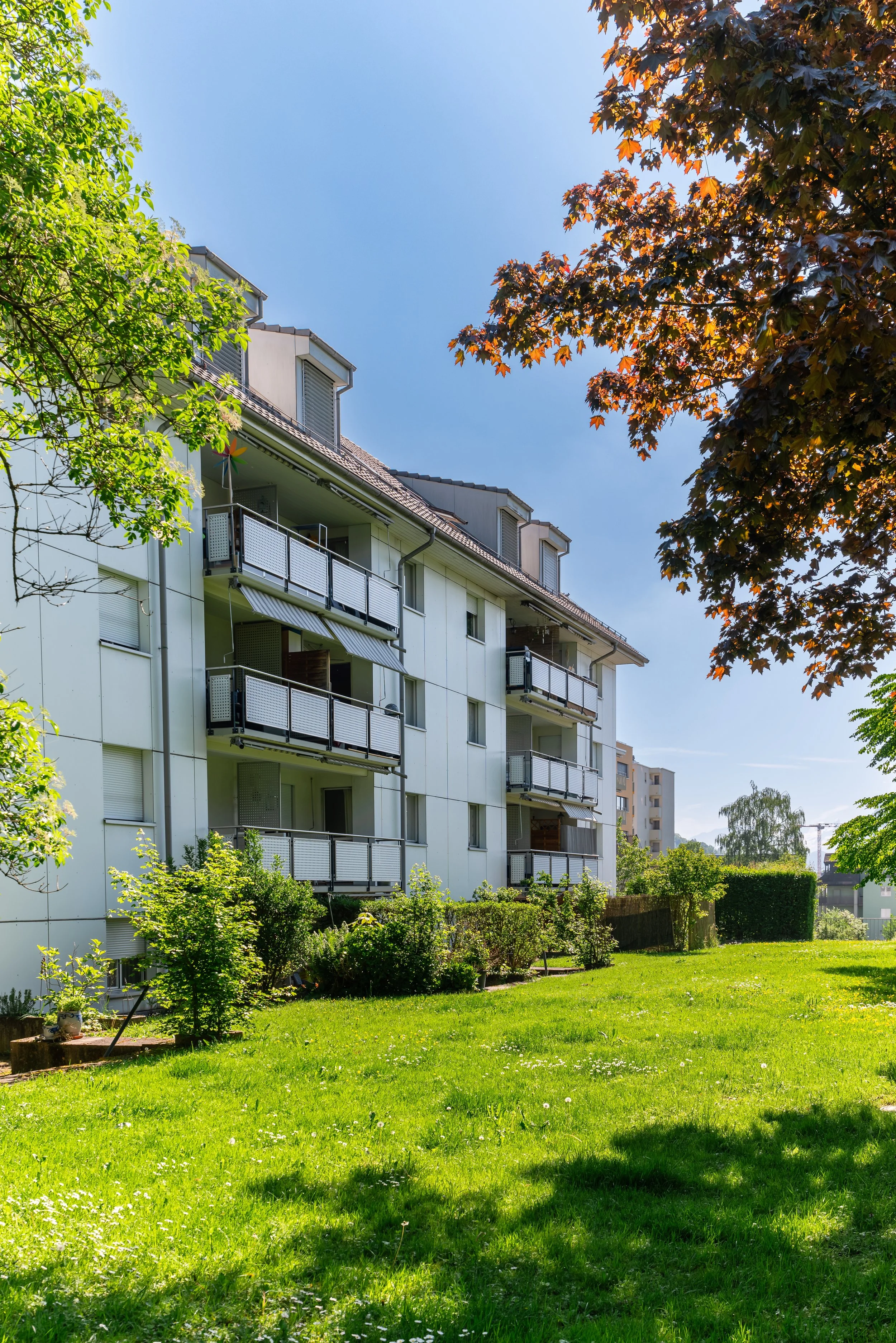 Sportweg 6/8, Kriens - Mehrfamilienhaus mit Balkonen in einer grünen Gartengegend bei sonnigem Wetter, im Hintergrund weitere Wohngebäude.