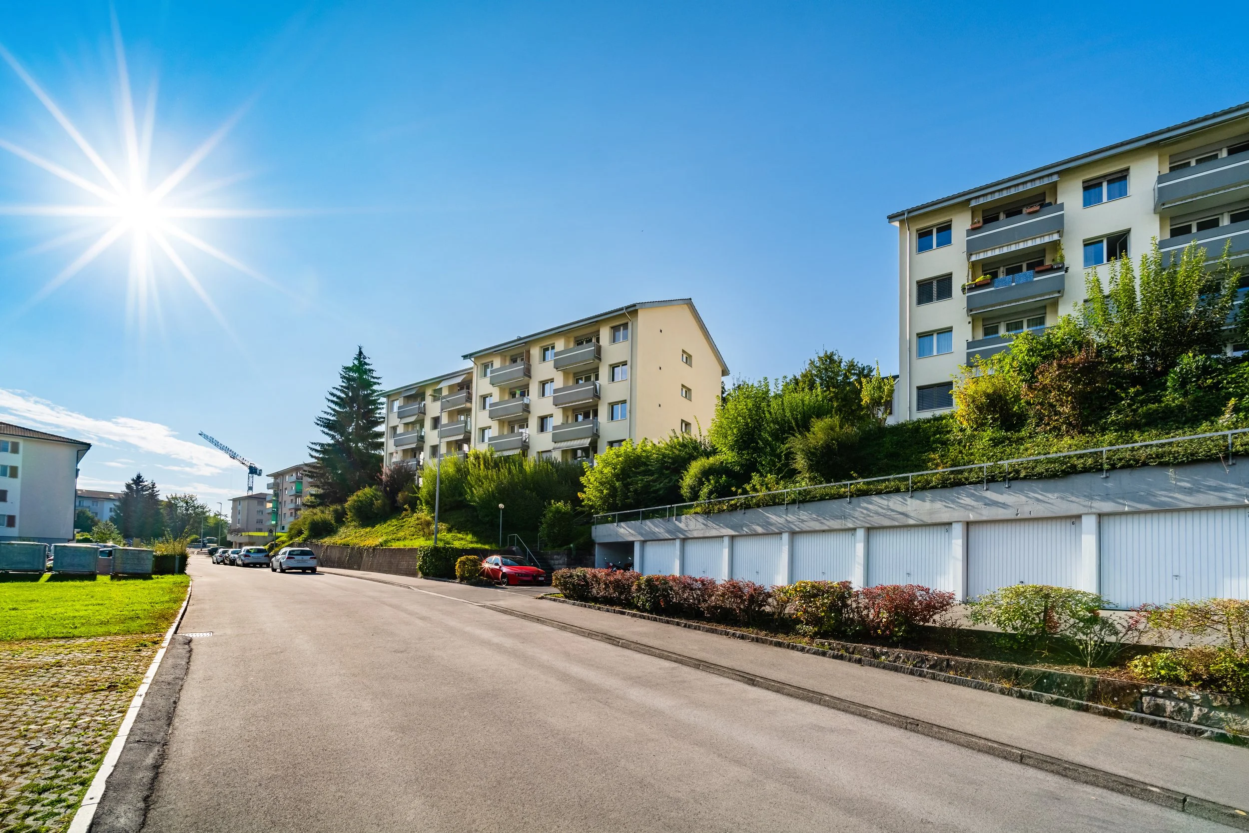 Buchfeldstrasse 15-21, Buchrain - Eine ruhige Straße in einem Wohnviertel mit mehrstöckigen Apartments, sonnigem Himmel und grünen Büschen.