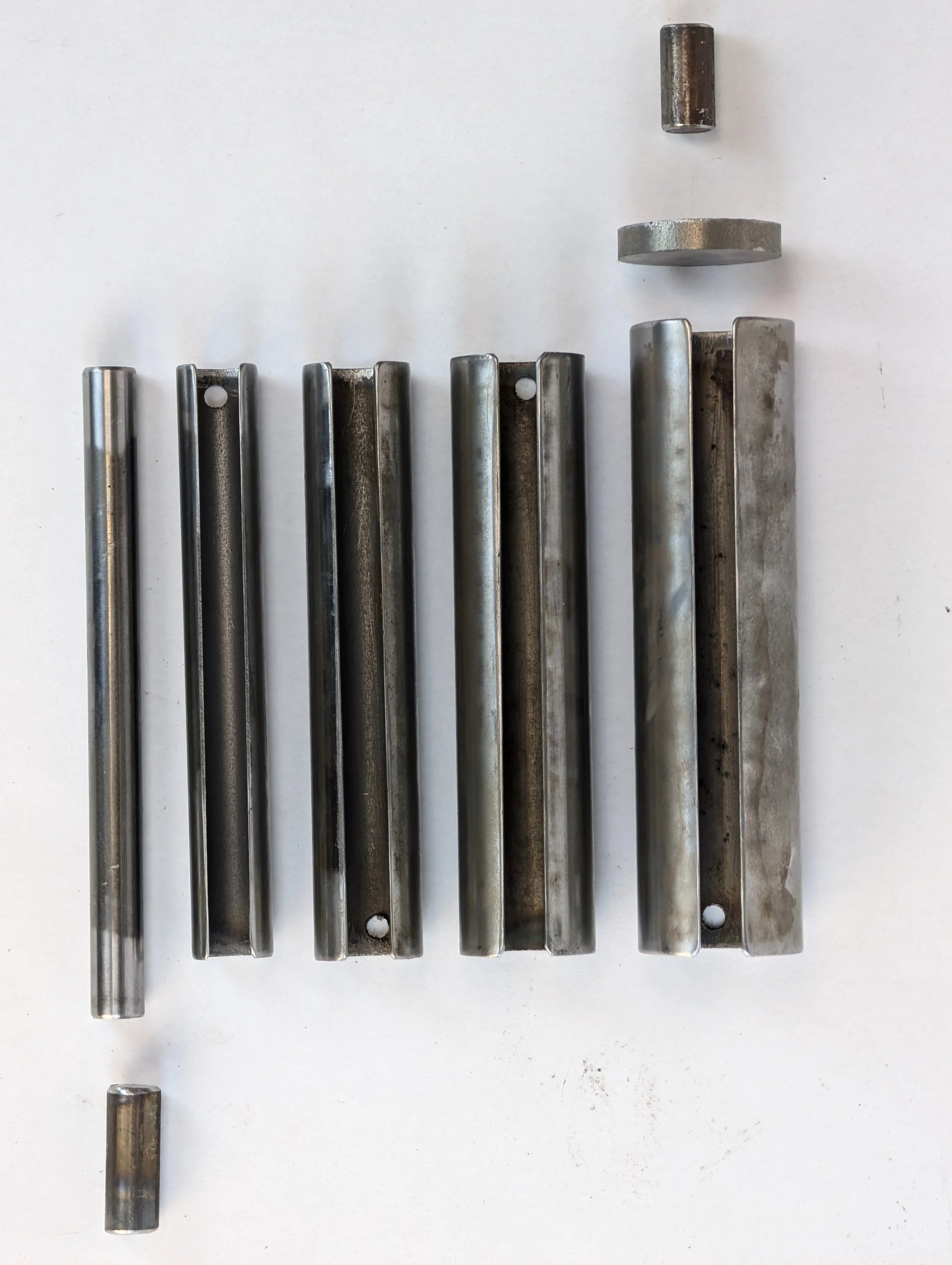 Collection of metal mechanical parts, including rods and caps, arranged on a white surface.