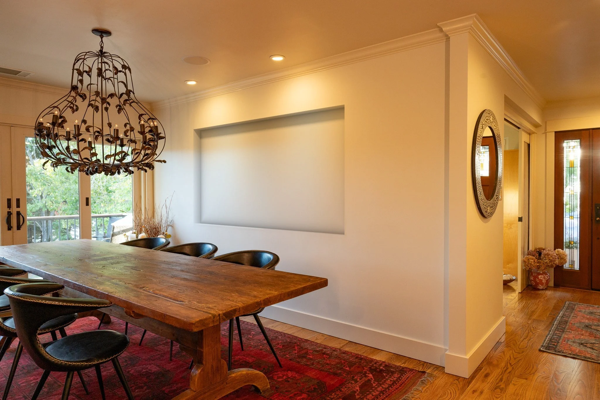 Dining room with a long wood table and an ornate chandelier, and an empty recessed niche in the far wall.