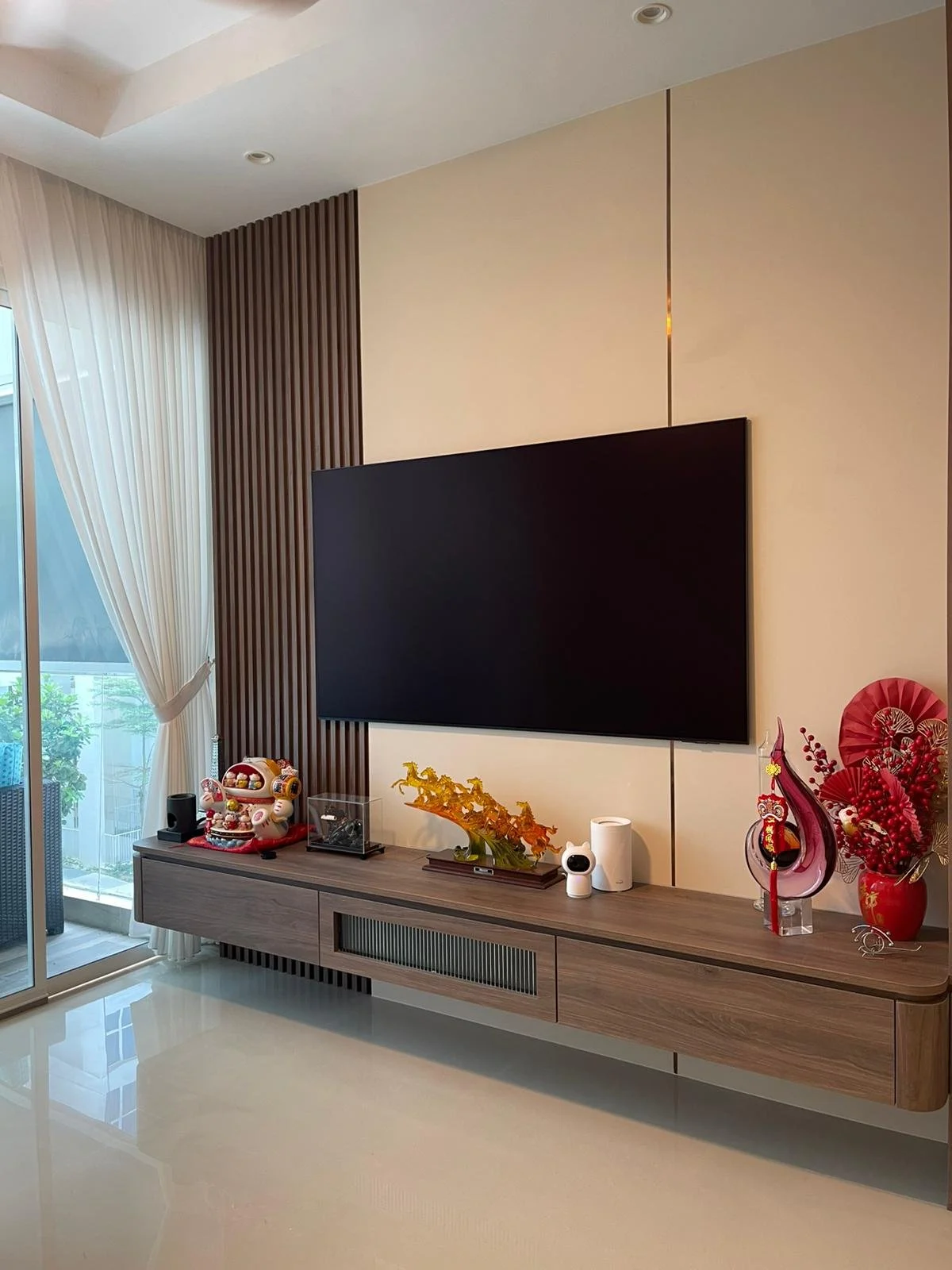 Modern living room with a wall-mounted flat-screen TV and a wooden TV console decorated with colorful festive ornaments and decorations.